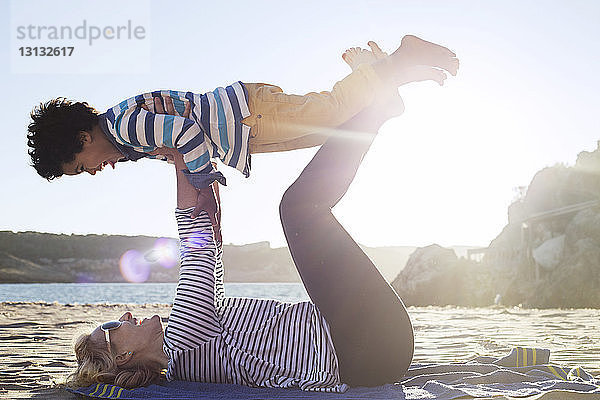 Seitenansicht einer Mutter  die an einem sonnigen Tag mit ihrem Sohn am Strand spielt
