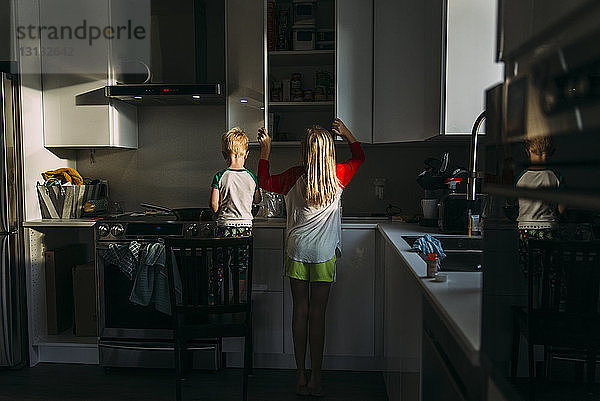 Rückansicht von Geschwistern  die zu Hause in der Küche stehen