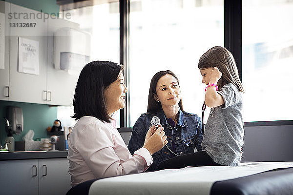 Seitenansicht eines Mädchens  das ein Stethoskop trägt  während der Arzt und die Mutter sie in der Klinik anschauen