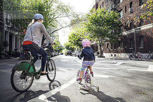 Rückansicht von Mutter und Tochter beim Fahrradfahren auf der Straße