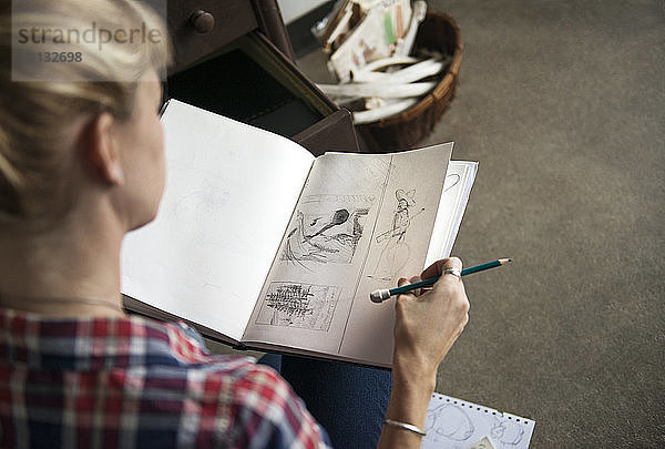 Künstlerin betrachtet Skizzen in Buch  während sie zu Hause sitzt