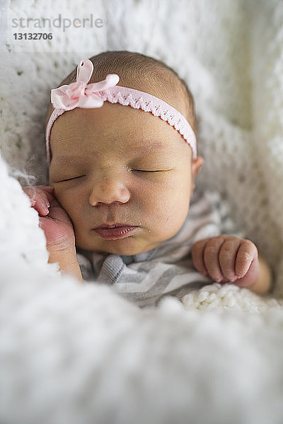 Nahaufnahme eines süßen neugeborenen Mädchens mit Stirnband  das zu Hause auf dem Bett schläft