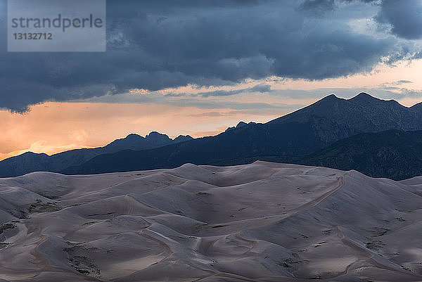 Landschaftliche Ansicht von Wüste gegen Berge und stürmische Wolken im Great Sand Dunes National Park