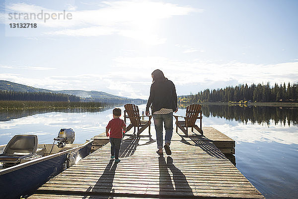 Rückansicht von Mutter und Sohn beim Spaziergang auf dem Holzsteg über den See gegen den Himmel
