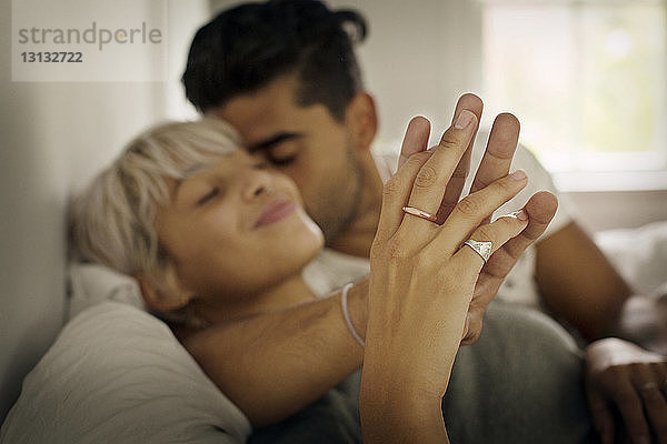 Zärtlicher junger Mann küsst Frau  während er im Schlafzimmer die Hand hält
