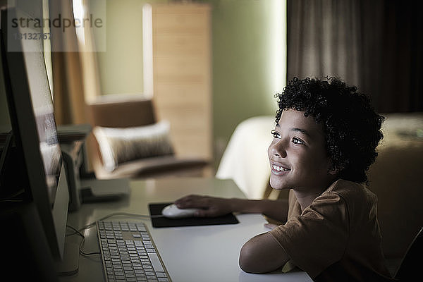 Lächelnder Junge  der zu Hause am Computer sitzt