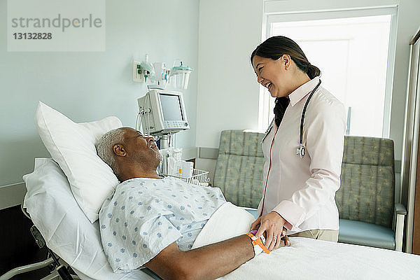 Fröhlicher Arzt im Gespräch mit älterem Patienten  der auf der Krankenhausstation im Bett liegt