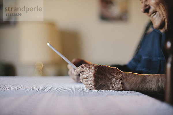 Beschnittenes Bild eines älteren Mannes  der einen Tablet-Computer am Tisch hält