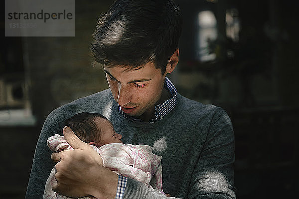 Vater schaut beim Tragen der neugeborenen Tochter zu Hause