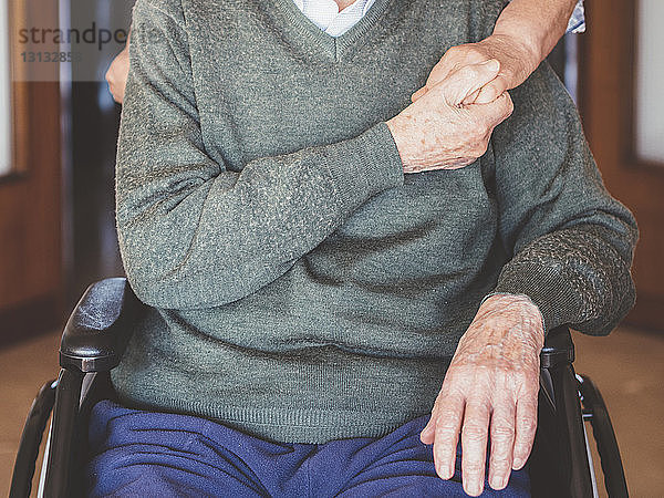 Mittelteil eines älteren Mannes  der eine Frau an der Hand hält  während er auf einem Rollstuhl sitzt
