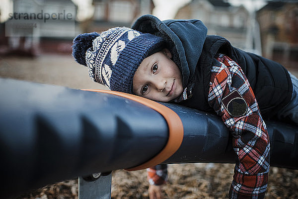 Porträt eines süßen Jungen  der auf einem Spielgerät im Freien auf dem Spielplatz liegt