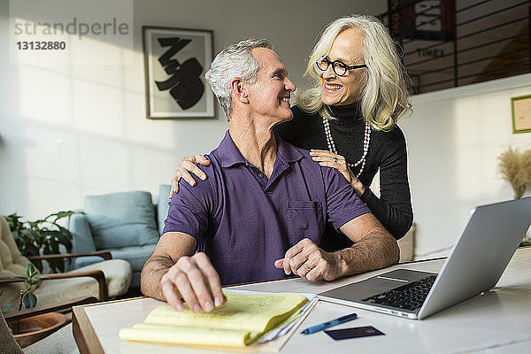Lächelndes Paar  das sich bei der Benutzung eines Laptops zu Hause von Angesicht zu Angesicht gegenübersteht