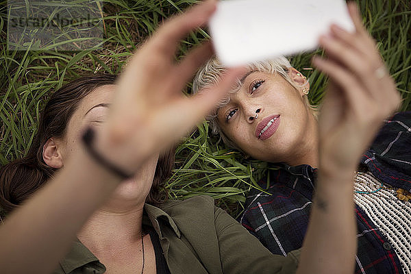 Freunde klicken mit dem Smartphone auf Selfie  während sie sich im Gras entspannen