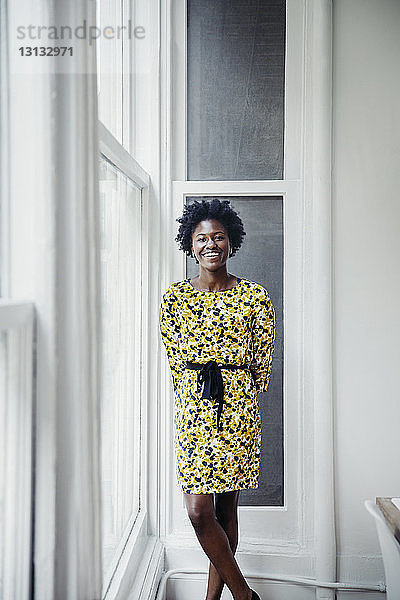 Porträt einer glücklichen Geschäftsfrau  die in einem kreativen Büro am Fenster steht