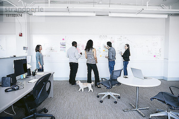 Geschäftsleute schreiben Notizen auf weißer Tafel und diskutieren im Büro