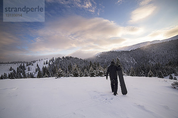 Rückansicht eines Mannes  der Skier trägt  während er auf einem verschneiten Berg läuft