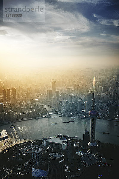 Luftaufnahme der modernen Stadtlandschaft am Huangpu-Fluss vor bewölktem Himmel bei Sonnenuntergang