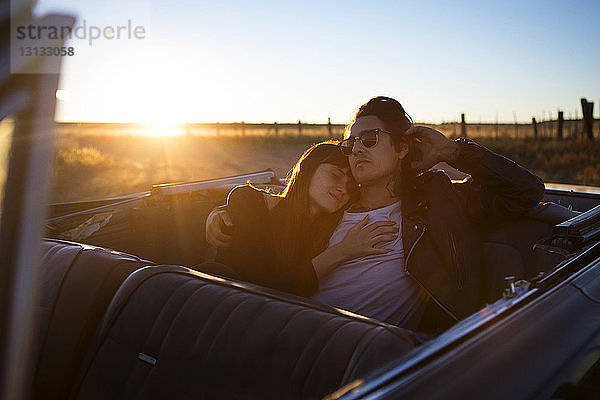 Paar entspannt sich bei Sonnenuntergang auf dem Rücksitz im Cabrio