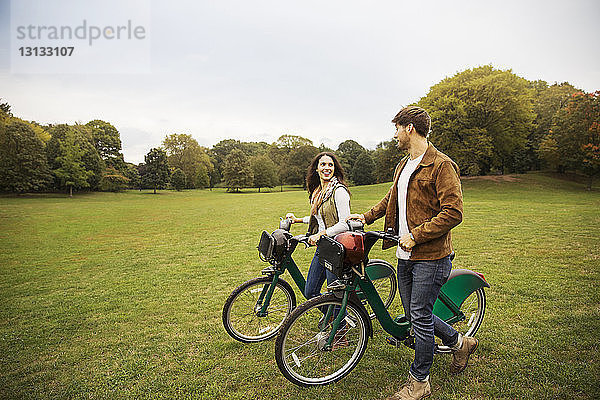 Glückliches Paar unterhält sich beim Spaziergang mit Fahrrädern auf einer Wiese