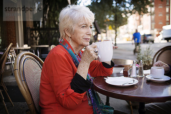 Ältere Frau schaut beim Kaffeetrinken im Straßencafé weg