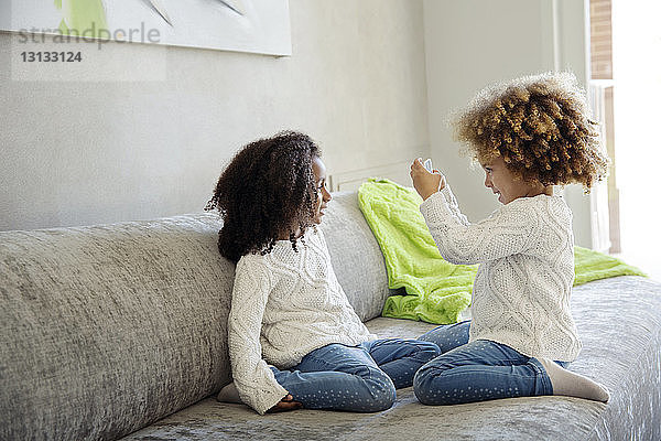 Mädchen fotografiert Schwester mit Smartphone auf Sofa