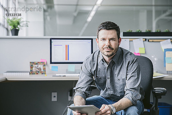 Porträt eines Geschäftsmannes mit Tablet-Computer auf einem Stuhl im Büro sitzend