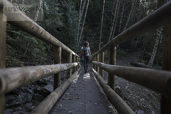 Rückansicht einer Frau  die auf einer Holzbrücke im Wald geht