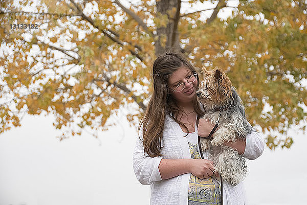 Niedrigwinkelansicht eines Mädchens  das einen Hund trägt  während sie im Herbst im Park an einem Baum steht