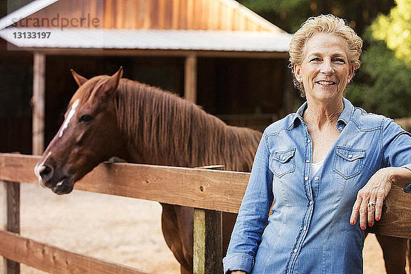 Lächelnde ältere Frau steht beim Pferd auf dem Bauernhof