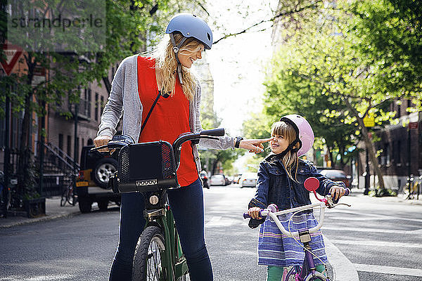 Glückliche Frau berührt die Nase ihrer Tochter  während sie mit dem Citi Bike auf der Straße steht