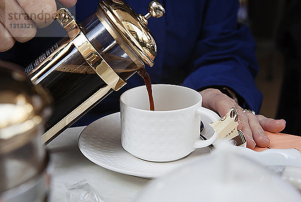 Beschnittenes Bild von Händen  die Kaffee in eine Tasse gießen