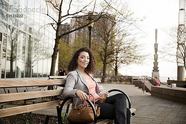 Porträt einer glücklichen Geschäftsfrau  die auf einer Bank am Fussweg sitzt