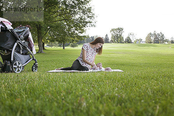 Mutter spielt mit dem Baby  während sie sich auf dem Grasfeld im Park ausruht