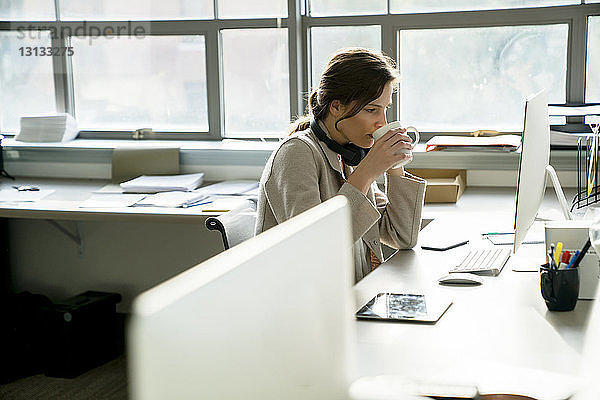 Seitenansicht einer Geschäftsfrau  die während der Arbeit am Schreibtisch im Büro trinkt