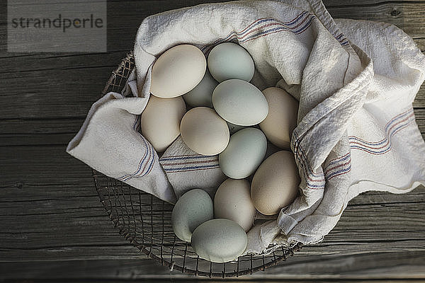Draufsicht von Eiern auf Textil im Korb am Holztisch