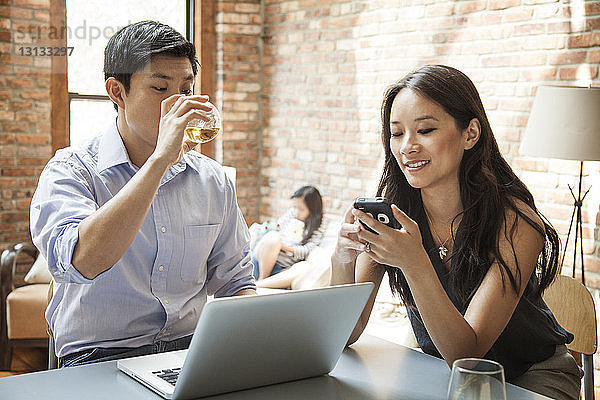 Frau benutzt Smartphone  während sie mit ihrem Mann am Tisch sitzt