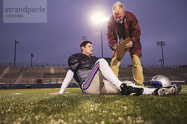 Trainer zeigt müden American-Football-Spielern  die sich auf dem Spielfeld im Stadion entspannen  die Zwischenablage