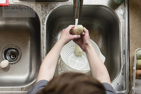 Hochwinkelaufnahme eines Jungen  der in der Küche ein Ei mit Wasser putzt