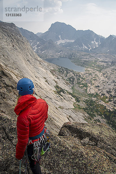 Hochwinkelaufnahme einer Wanderin mit Bergsteigerausrüstung  die auf einer Klippe gegen den Himmel steht