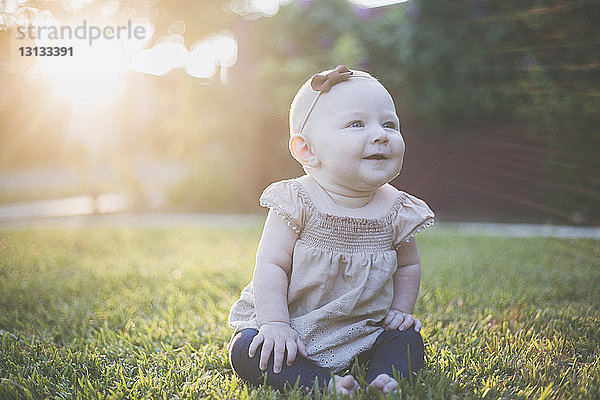 Glückliches kleines Mädchen schaut weg  während es auf einem Grasfeld im Hinterhof sitzt