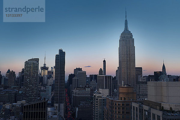 Empire State Building inmitten des Stadtbildes vor klarem blauen Himmel in der Abenddämmerung