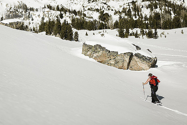 Wanderin mit Rucksack besteigt schneebedeckten Berg mit Wanderstöcken