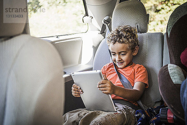 Glücklicher Junge benutzt Tablet-Computer  während er im Auto sitzt
