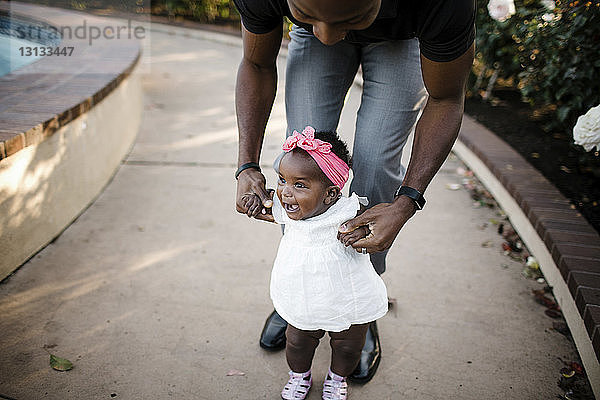 Vater hilft glücklicher Tochter beim Gehen auf Fußweg im Park