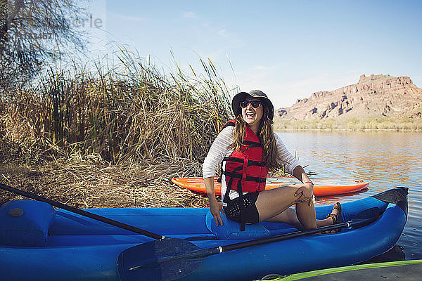 Glückliche Frau schaut weg  während sie auf einem aufblasbaren Kajak am Seeufer sitzt