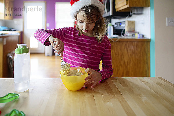 Mädchen mischt Futter in Schüssel  während sie zu Hause eine Nikolausmütze trägt