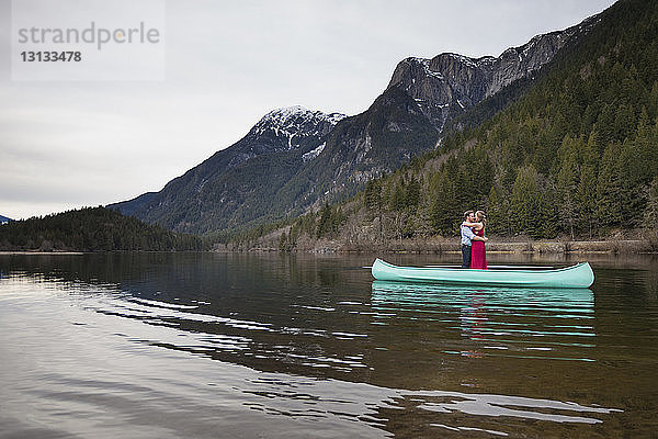 Junges Paar umarmt sich  während es im Kanu auf dem See vor den Bergen steht