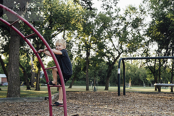 Lächelnder Junge klettert auf Spielplatz an Affenstangen