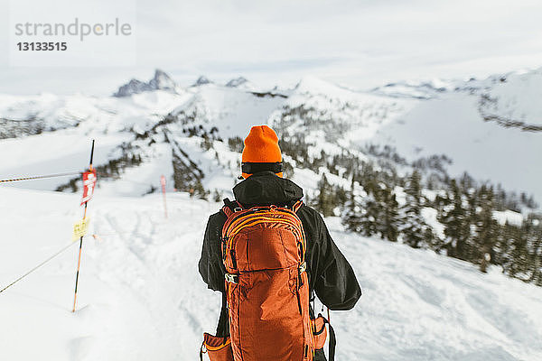 Rückansicht eines Wanderers mit Rucksack auf einem schneebedeckten Berg während eines Skiurlaubs