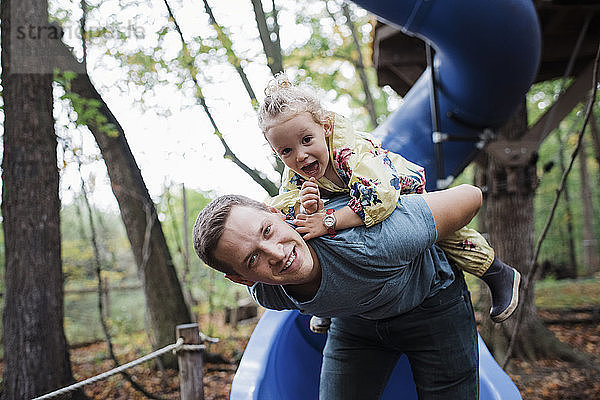 Porträt eines Vaters  der seine Tochter auf dem Spielplatz huckepack nimmt